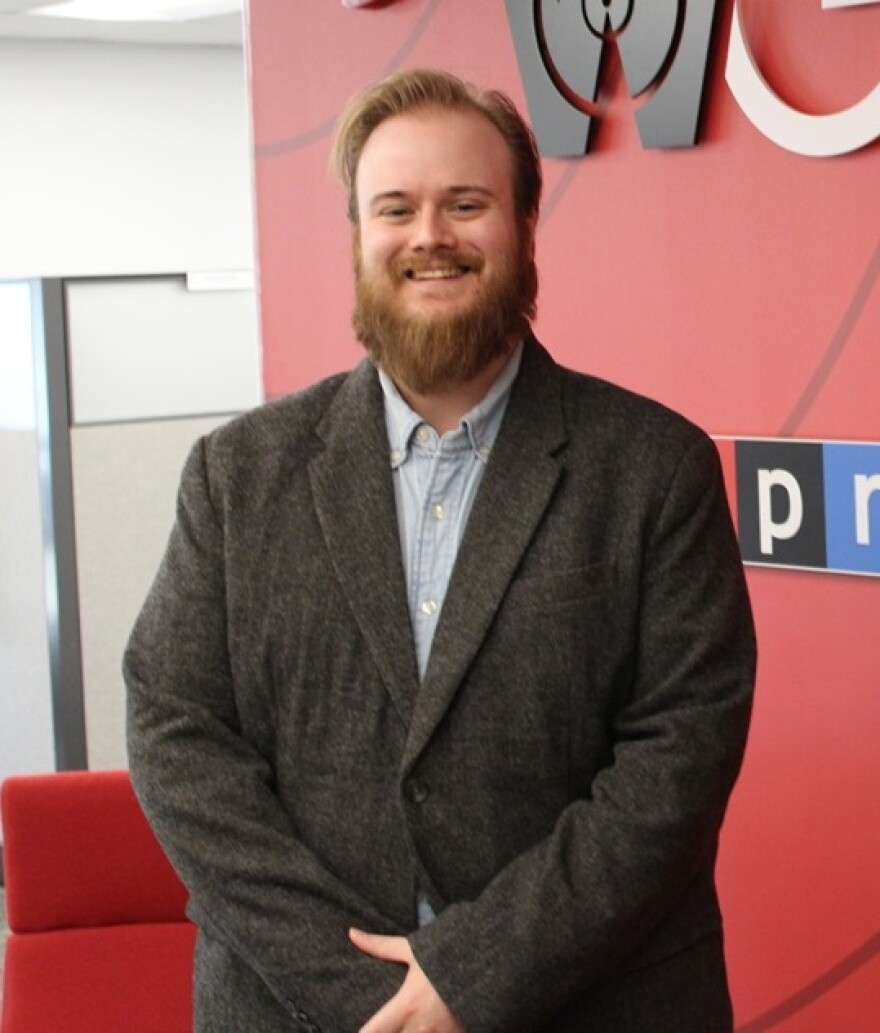 A man in a jacket poses for a photo in front of a sign that reads WGLT