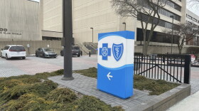 A blue and white sign with the Blue Cross Blue Shield logo stands in a grassy patch in front of a large grey building.