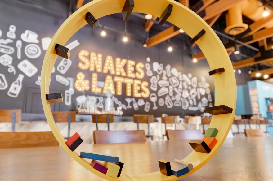 sign says snakes & lattes on wall surrounded by games and seats