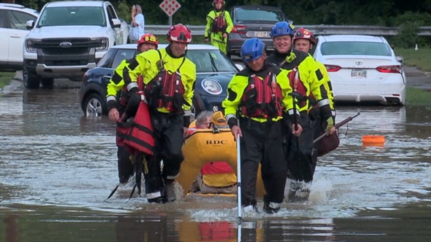 5 men in safety gear carry an inflatable boat that holds another person through ankle-deep water