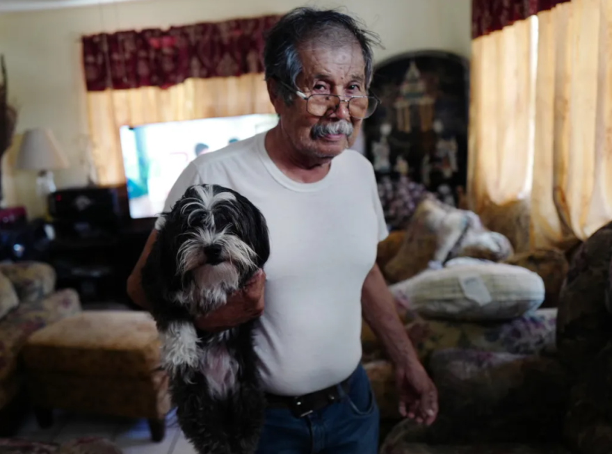 Arturo Gómez, 80, carries one of his three dogs through his home in July in La Lomas Colonia in Rio Grande City, Texas, where they all suffer from the rising temperatures and high cost of electricity.