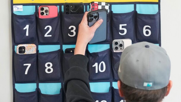 FILE - A ninth grader places his cellphone into a phone holder as he enters class at Delta High School, Friday, Feb. 23, 2024, in Delta, Utah. (AP Photo/Rick Bowmer, file)