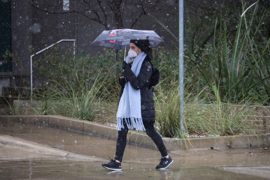 A pedestrian walks by the UT Austin campus as it snows.