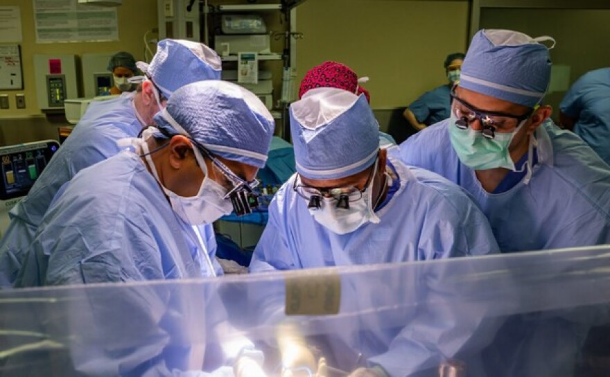 Surgeons hover over a patient in an operating room.
