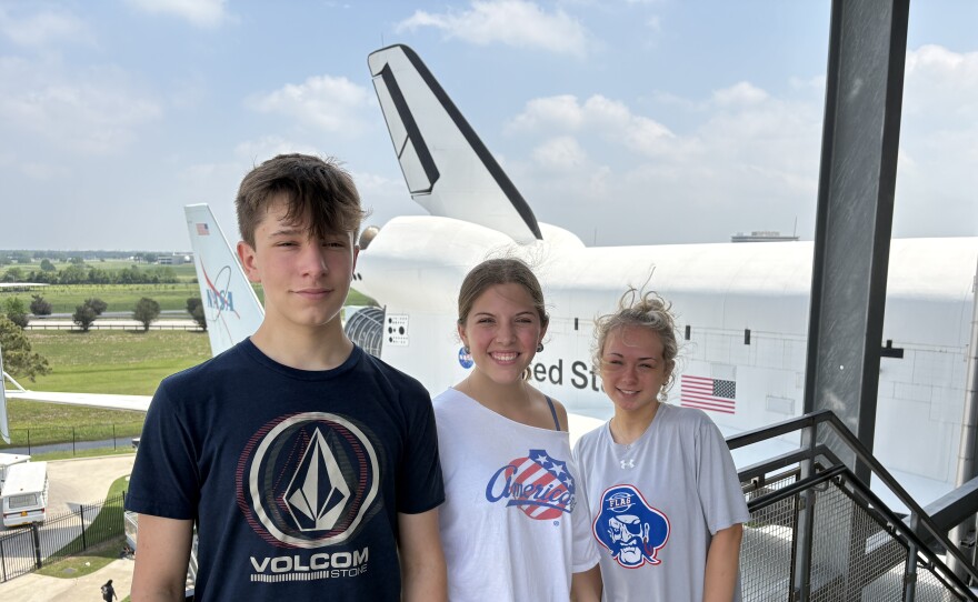 Three young people stand in front of a large plane.