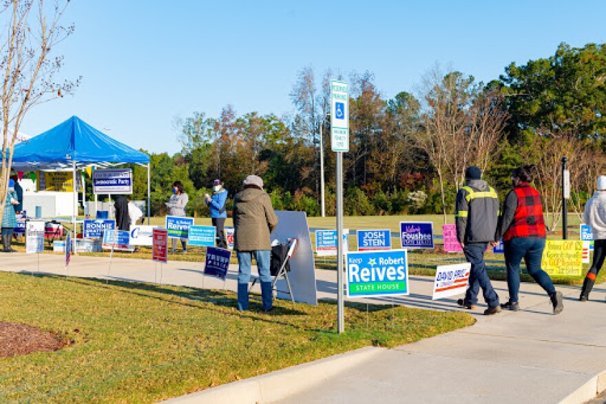 A Pittsboro polling place with scattered individuals and a thicket of political signage.