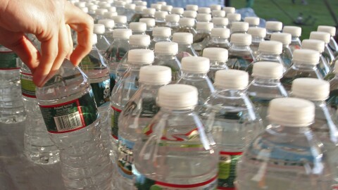 A hand grabs a bottle of water from a table.