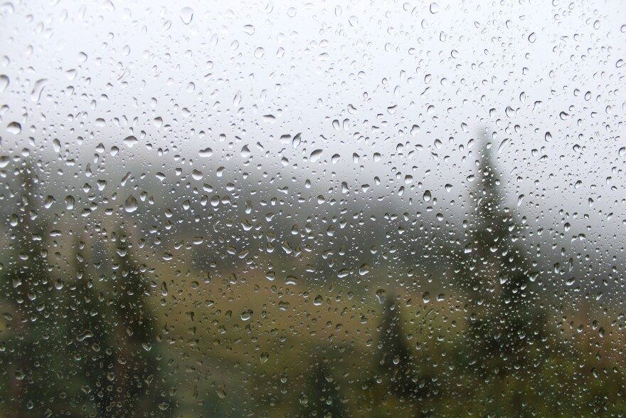 water droplets form on glass with a view of clouds, mountains, and trees in the background