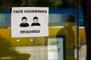 Sign on a door with a drawing of two people wearing face masks that says "face coverings required"