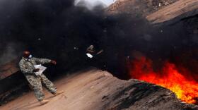 An Air Force master sergeant tosses unserviceable uniform items into a burn pit at Balad Air Base, Iraq, on March 10, 2008. 