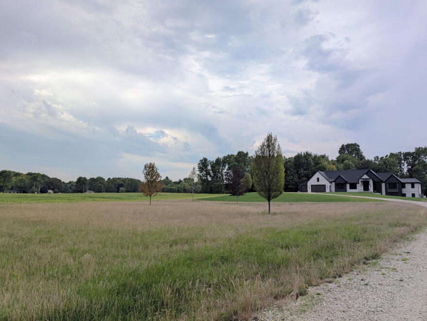 A house is seen at the end of a gravel driveway with a large field to the left of it