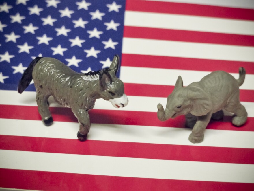 figurines of a gray donkey and a gray elephant stand on the american flag