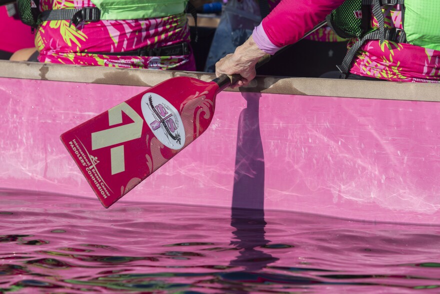 A woman holds a pink dragon boat oar with a breast cancer awareness ribbon on it.