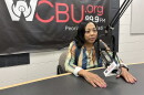 A woman speaks into a radio microphone in front of a WCBU 89.9 FM banner.