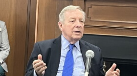 U.S. Senator Dick Durbin sitting at a round table with a microphone on it. His shirt is light blue. His tie is vibrant cerulean. 