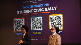 Two students speaking in front of a screen.