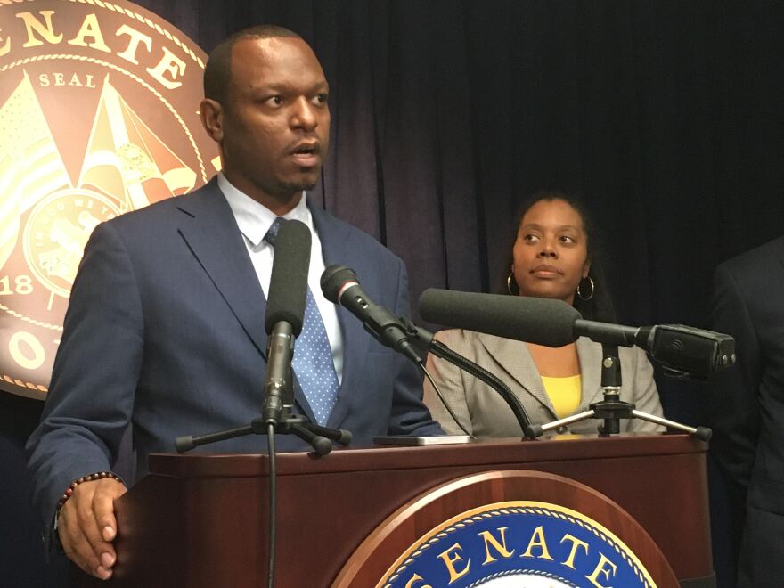 Man in suit and tie stands at a podium. A woman in a blazer stands next to him.