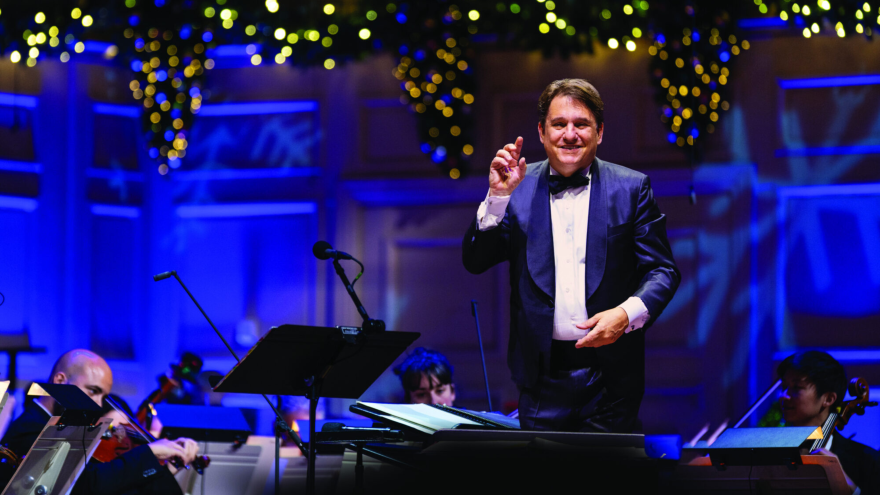 Keith Lockhart conducting the Boston Pops, with glittering lights behind him.