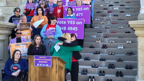 Domestic violence survivors and advocates Tanesha Ash-Shakoor, of Voices of Color, and Celeste Kanpurwalla, of Moms Demand Action, embrace on the western steps of the Michigan capitol on Thursday, September 14, 2023. Seventy empty pairs of shoes behind them represent the estimated 50 women and 20 children lost each year to firearm-related domestic violence.