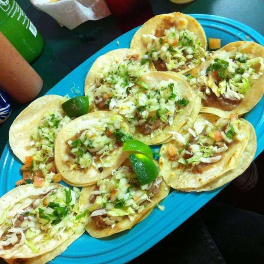 A pile of soft corn tortilla tacos on a bright blue plate. 