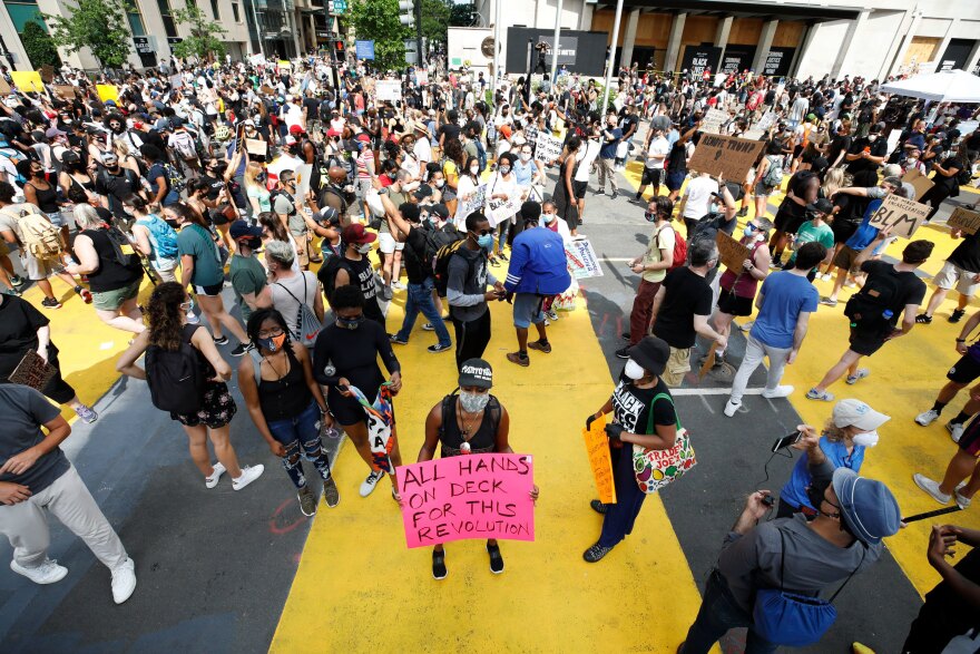 Protestors walk over a mural that reads "BLACK LIVES MATTER" in yellow capital letters down a two-block stretch of 16th street that Mayor Muriel Bowser officially renamed Black Lives Matter Plaza.