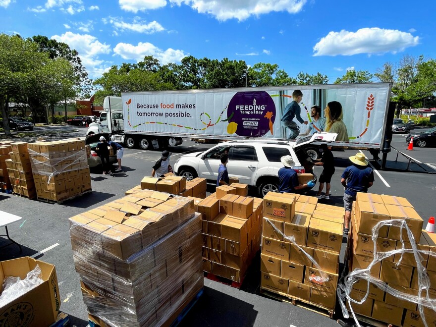 Pallets of boxes of food are in a parking lot being unloaded off of a truck by Feeding Tampa Bay staff.