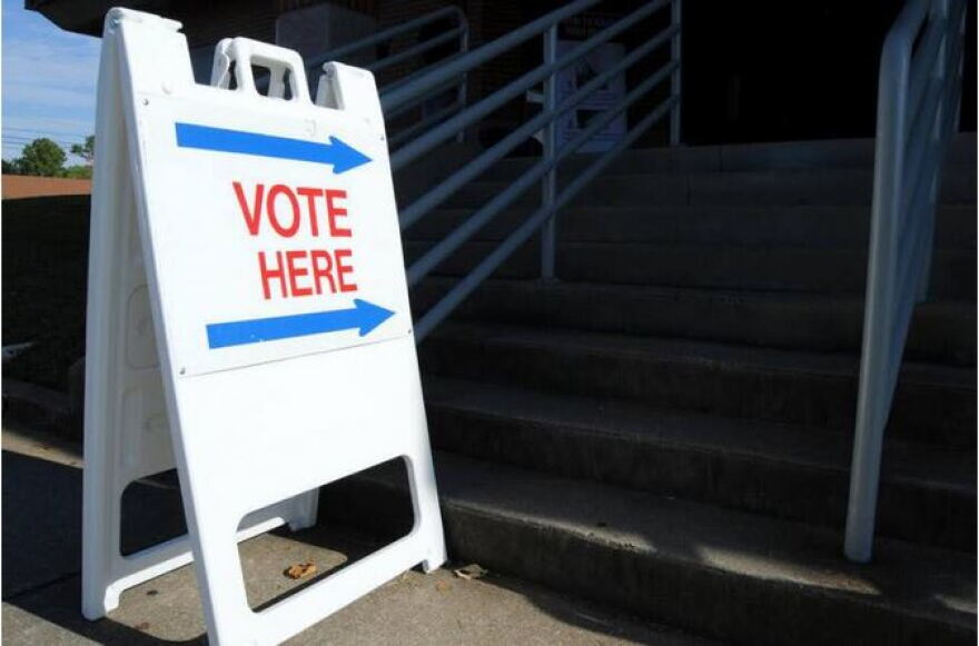 A white placard with the red words "VOTE HERE" and blue arrows on it, pointing up a stairway.