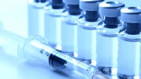 A syringe next to eight little glass bottles