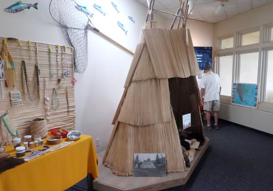An exhibit of a traditional thatched teepee made of light-beige sticks.