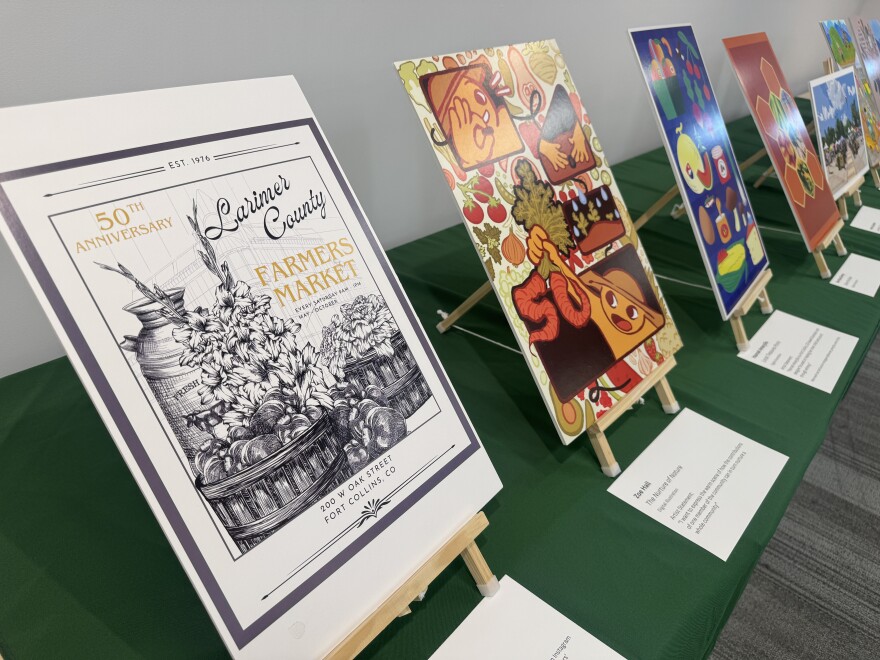 Several posters on small wooden easels sit on top of a green table. They all talk about the 50th Anniversary of the Larimer County Farmer's Market.