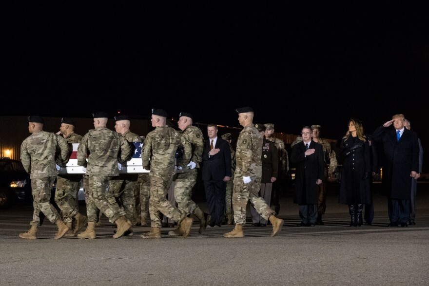 Soldiers carry coffin on tarmac while president solutes.
