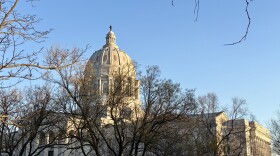 The dome of the Missouri state capitol building is visible through tree branches. 