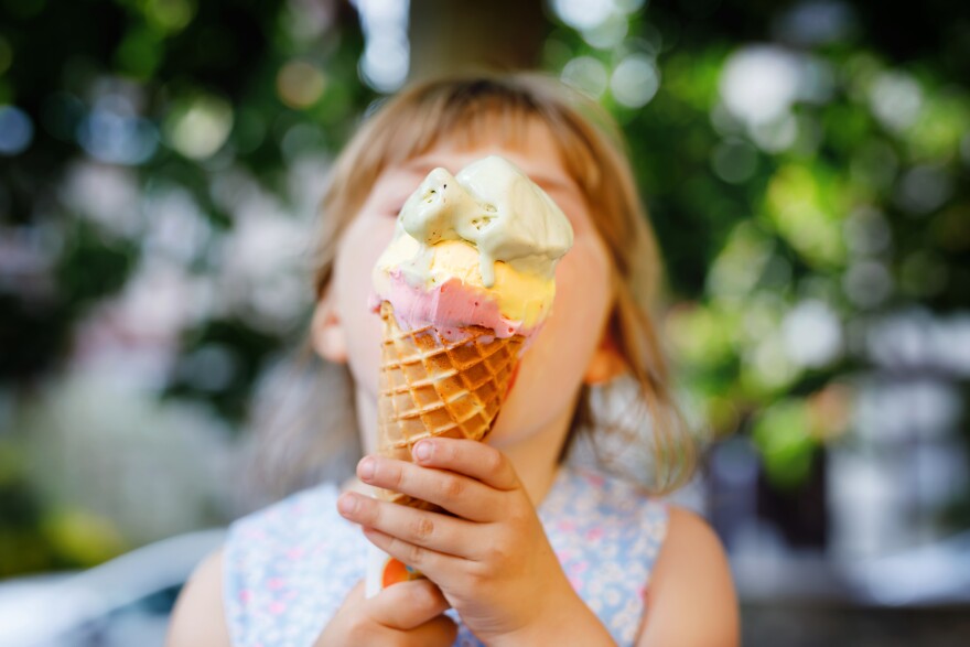 Little preschool girl eating ice cream in waffle cone on sunny summer day. Happy toddler child eat icecream dessert. Sweet food on hot warm summertime days. Bright light, colorful ice-cream.