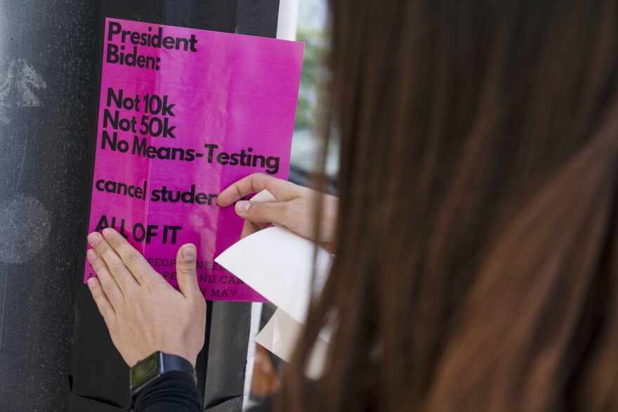 American University student Magnolia Mead puts up posters near the White House promoting student loan debt forgiveness, Friday, April 29, 2022, in Washington.