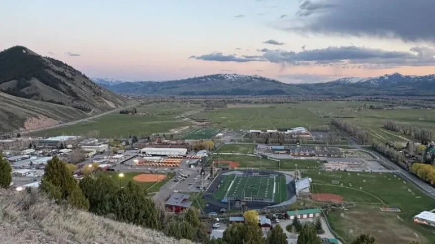 A photo taken from a hillside overlooking the town of Jackson. A track and football field are in the foreground, with mountains behind.