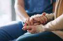 A senior woman holds hands with a nurse