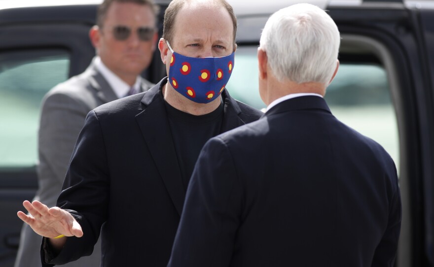Colorado Gov. Jared Polis wears a mask with the state's flag as he greets Pence in Colorado Springs.