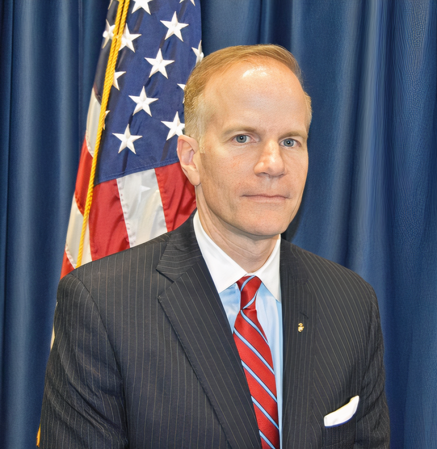 A head and shoulders photo of Bill McSwain in a jacket and tie with the American flag in the background.