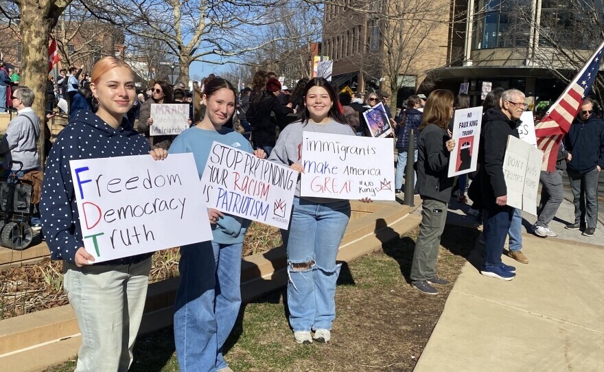 Three young women hold protest signs in Uptown Normal