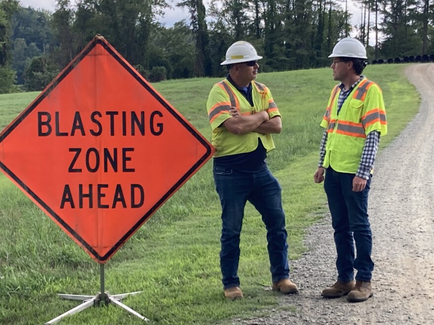 Inspector Travis Goode and spokesman Westley Kern stand by as the Rivanna Water and Sewer Authority prepares to blast through rock that's blocking a pipeline's path.