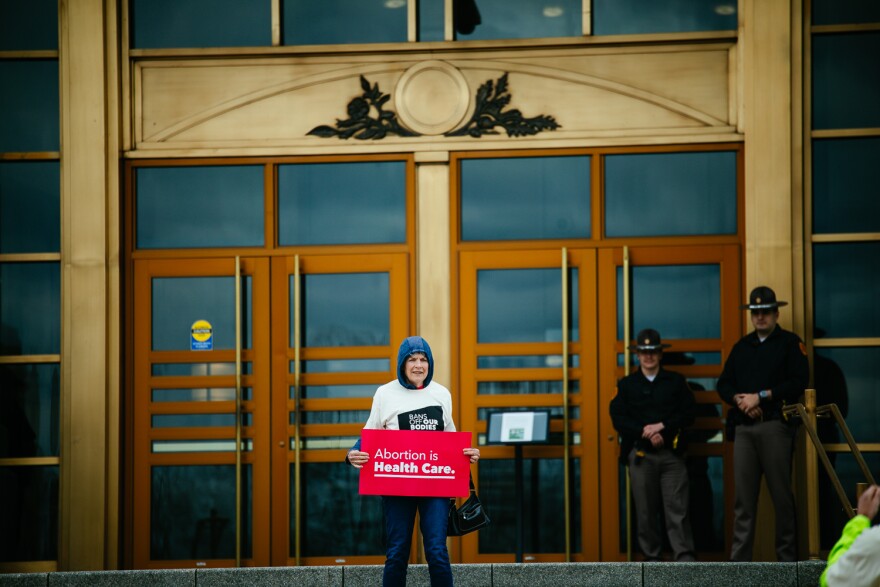Woman stands with sign reading "Abortion is Health Care" in front of security at the judicial building.