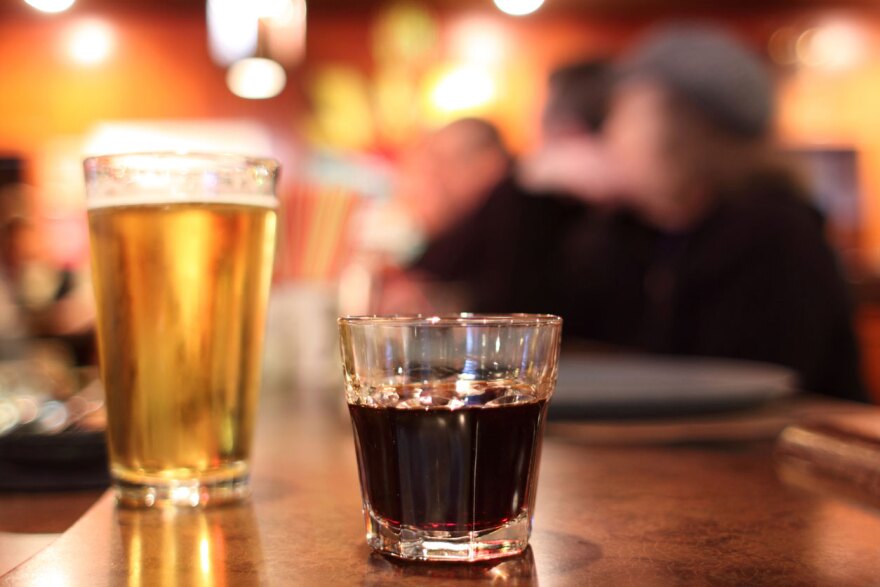 A beer and a shot of alcohol on a bar.