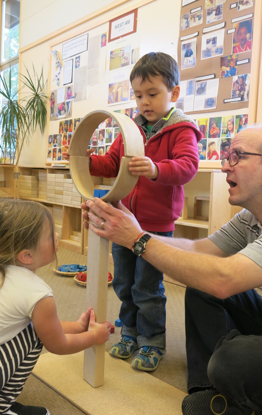 Four-year-olds Jacques and Corinne work with teacher Todd Erickson to balance and secure two semicircular wooden blocks atop two long, straight ones.