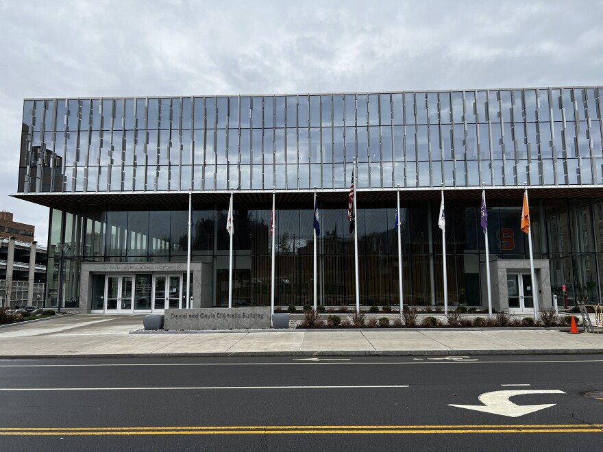 A glass building on a street with flagpoles in front of the entrance.