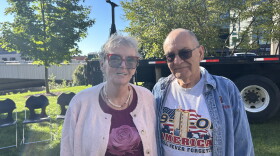 A man and woman stand together in a park. The man is wearing a 9/11 "Never Forget" shirt.
