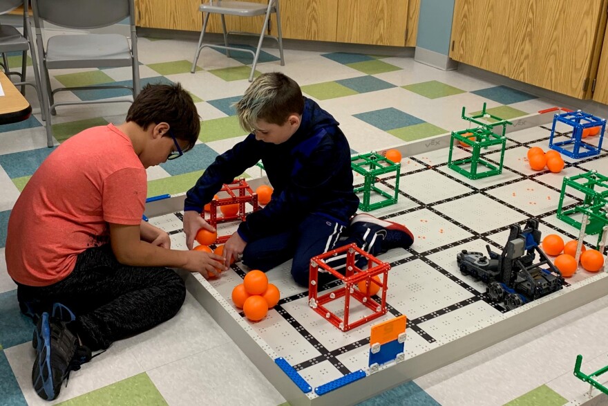 Two children sitting on the floor playing a game with cubes and orange balls. 