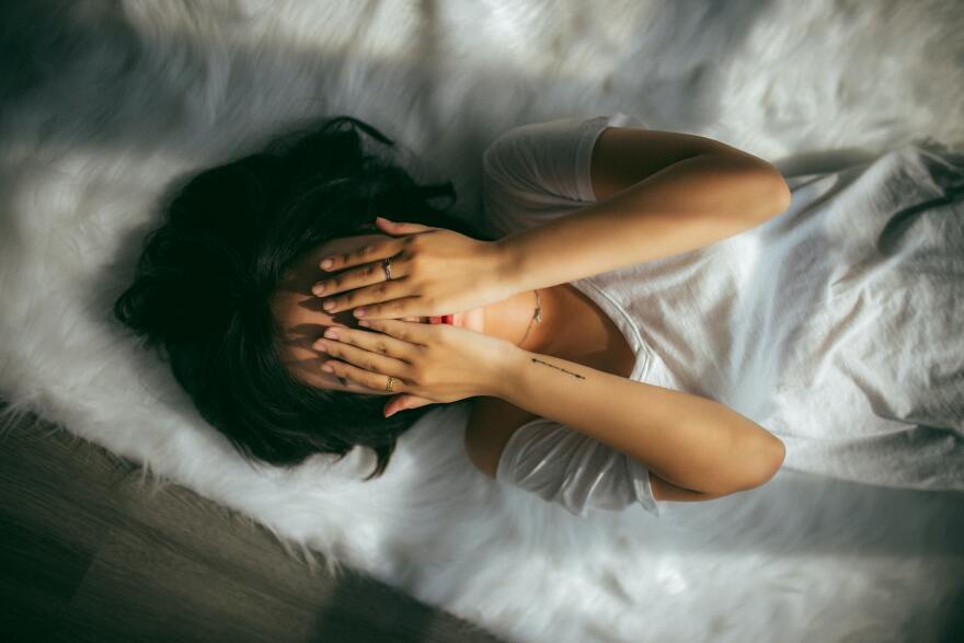 Woman lying on the bed with her hands covering her face.