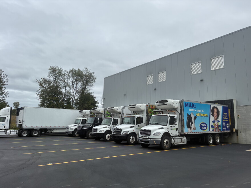 A photo outside of a warehouse with six food distribution box trucks parked outside of it 