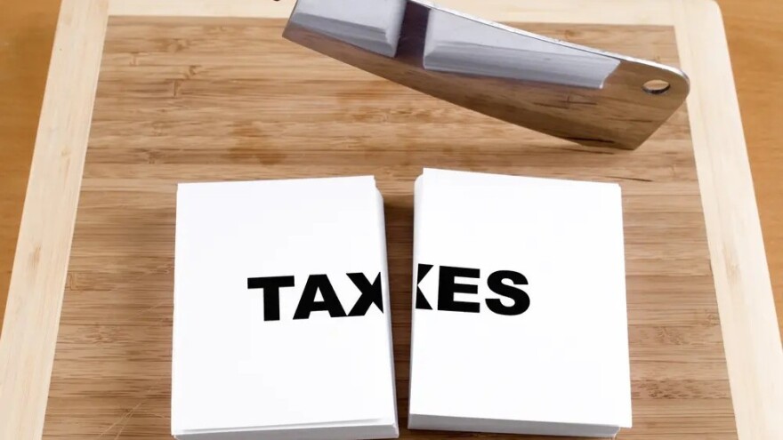 illustration shows an ax next to a stack of cards cut in half with the word TAXES written on the top card. Illustrates elimination or trimming of taxes 