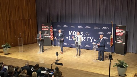 four men stand at podiums on a stage